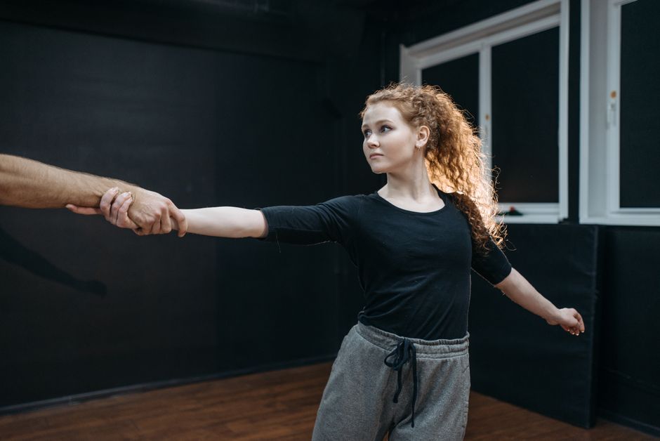 A young woman dancer holds hands with a partner during a ballet practice.