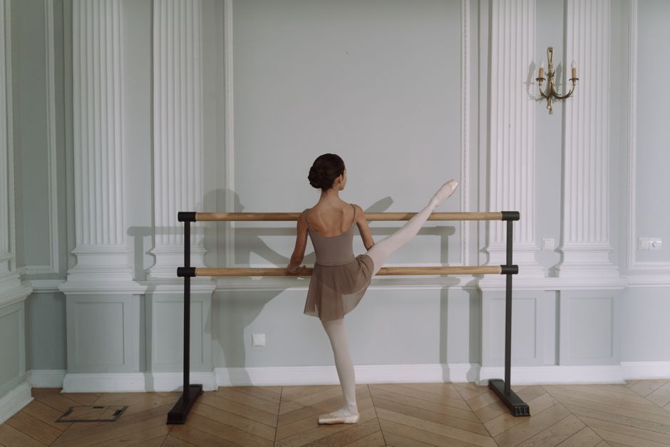 A young ballerina practices a leg stretch at a ballet barre in a classic studio.